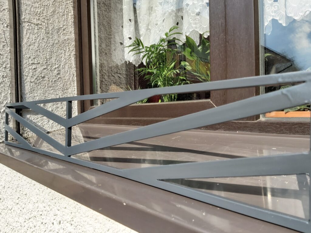 Solidna metalowa barierka z płaskowników atestowanej stali i nowoczesny kwietnik na parapet - styl i wytrzymałość.