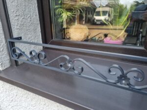 Solidna metalowa barierka z eleganckim wzorem roślinnym kwietnika na parapet - połączenie estetyki i funkcjonalności.