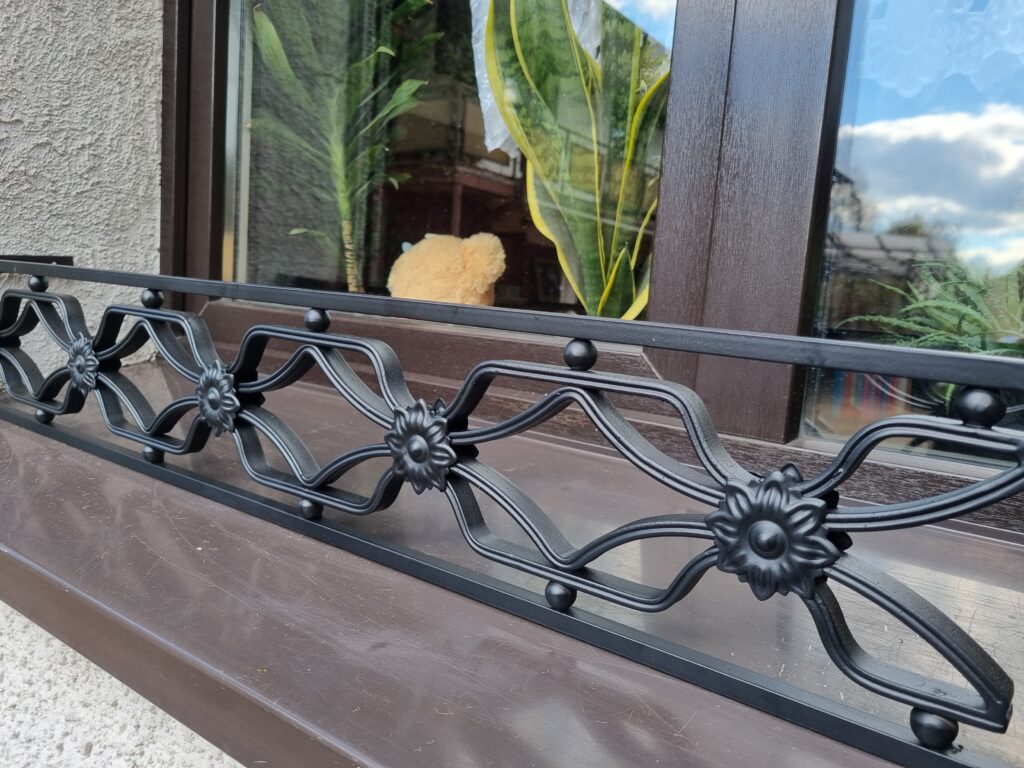 Solidna metalowa barierka z bogatymi ornamentami - eleganckie i wytrzymałe zabezpieczenie dla Twojego parapetu.