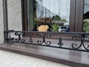 Solidny metalowy kwietnik na parapet zewnętrzny, zapewniający ochronę roślinom przed silnymi wiatrami.
