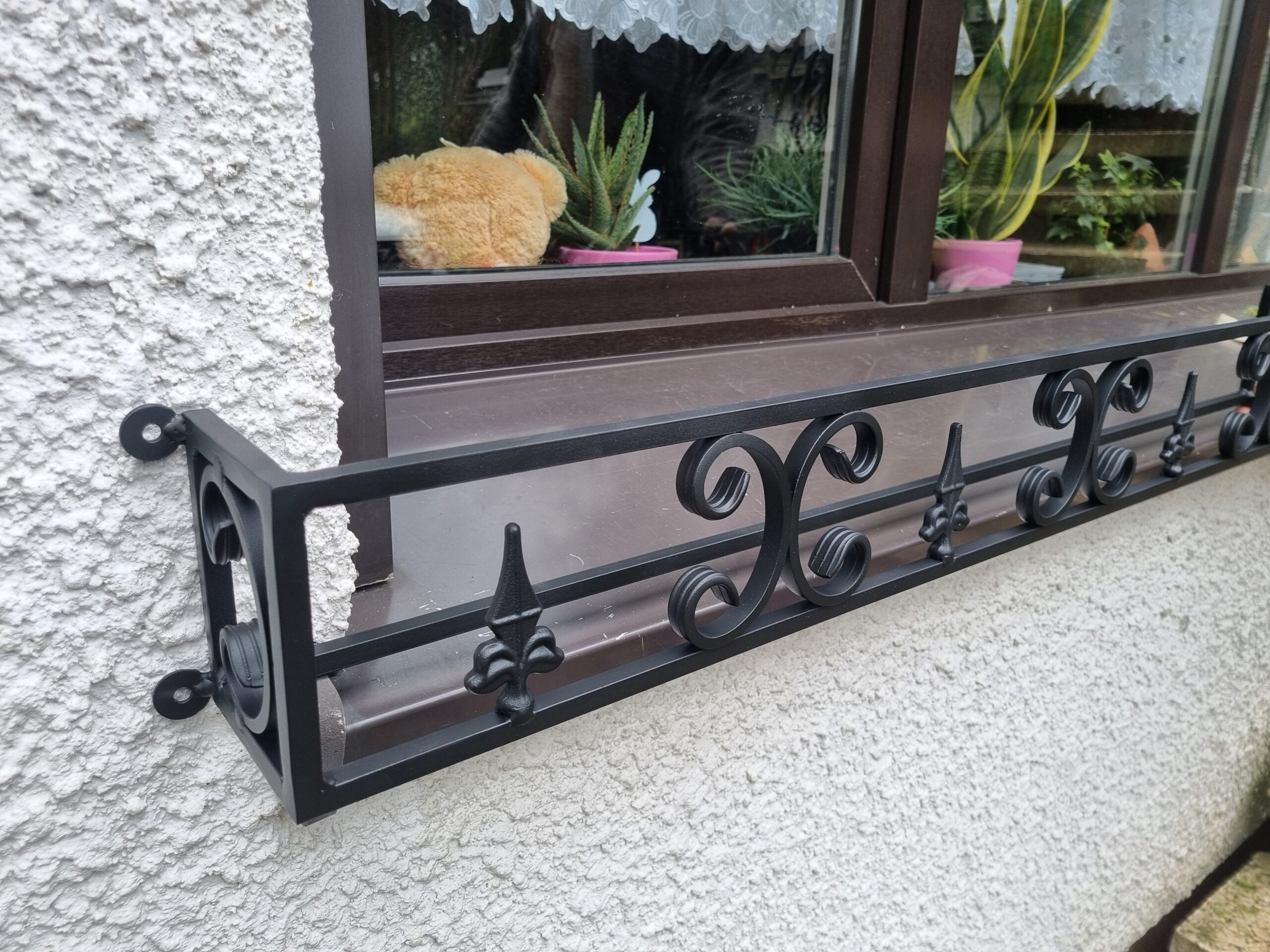 Solidny metalowy kwietnik na zewnętrzny parapet, idealna ochrona roślin przed silnymi wiatrami.