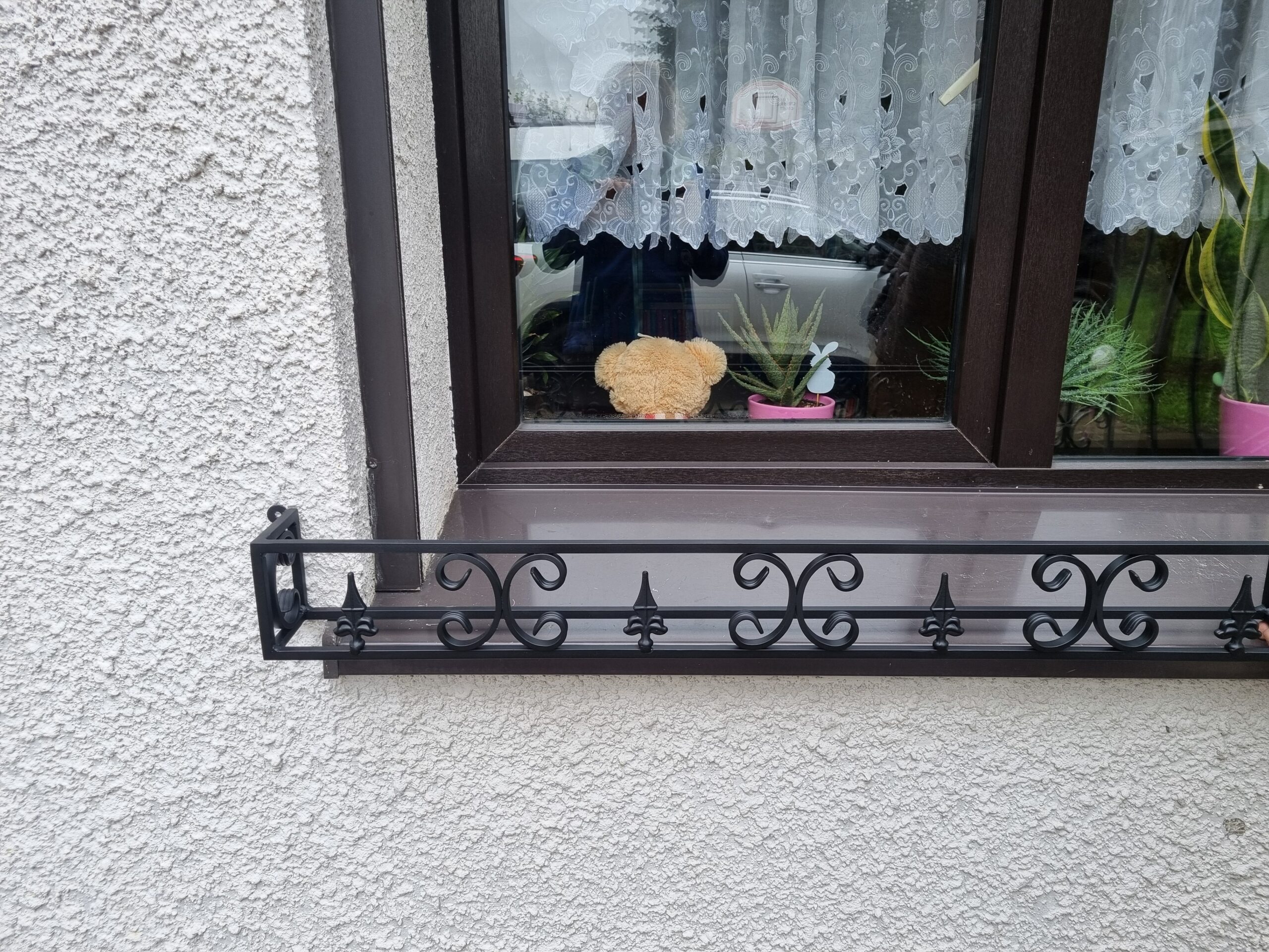 Solidny metalowy kwietnik na parapet zewnętrzny, idealny do ochrony roślin przed wiatrem i deszczem.